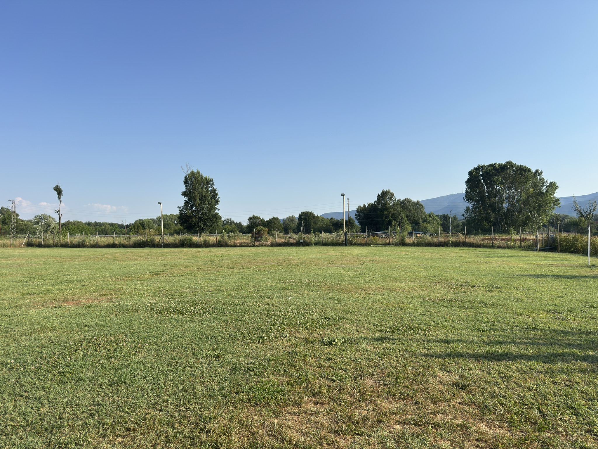 Vista panoramica del campo verde, con alberi e colline sullo sfondo